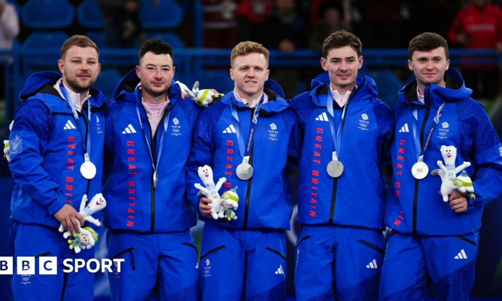 From left, Kyle Waddell, Hammy McMillan, Bobby Lammie, Grant Hardie and Bruce Mouat standing on the podium with their silver medals. They are all wearing blue Great Britain tracksuits.