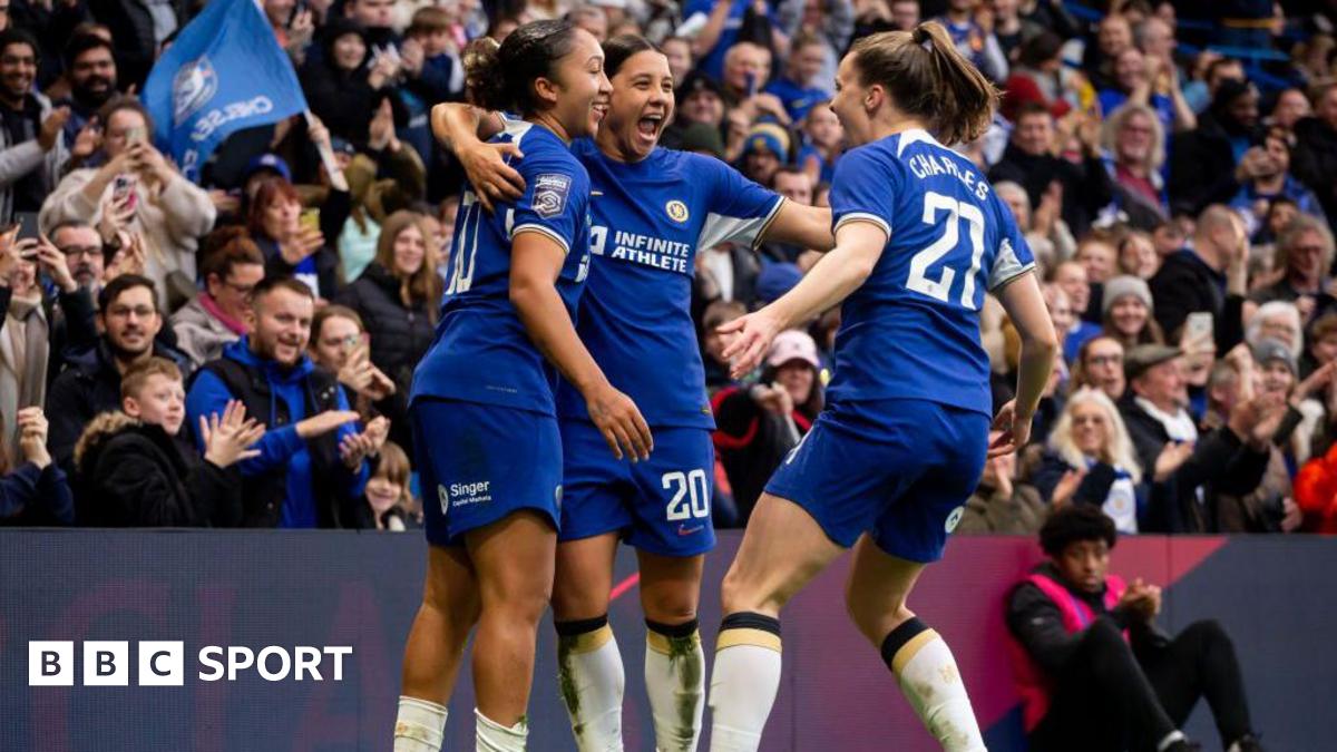 Lauren James celebrates scoring at Stamford Bridge as Sam Kerr and Niamh Charles join her in a huddle, with fans applauding in the stand behind them