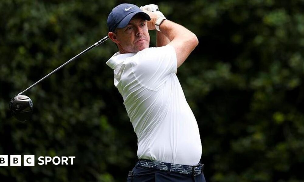 Rory McIlroy at the Truist Championship, wearing a white golf shirt and blue cap, swinging a metal wood