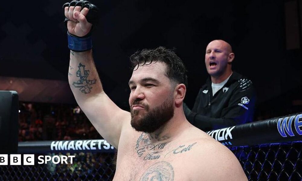 Louie Sutherland holds up his arm as he stands in the octagon
