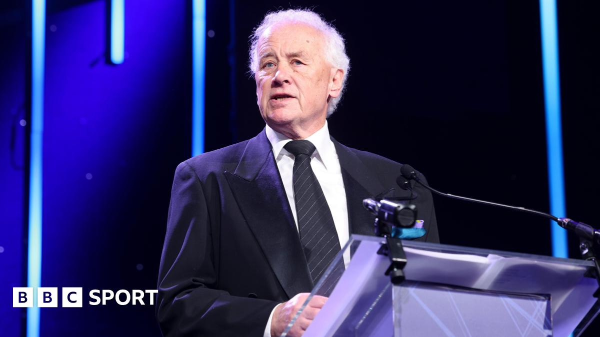 Ricky Parry wearing a blue suit jacket, white shirt and black tie with silver diagonal stripes standing behind a lectern addressing the EFL awards ceremony
