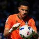 Pierce Charles concentrates on catching the ball in his hands, wearing orange goalkeeping jersey