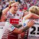 Wigan Warriors player Taylor Kerr, number 25 with his back to camera, is embraced and congratulated by team-mates after scoring a try.