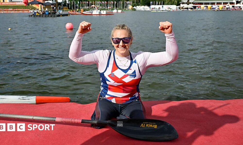 Charlotte Henshaw celebrates with her arms raised having just got out of her kayak