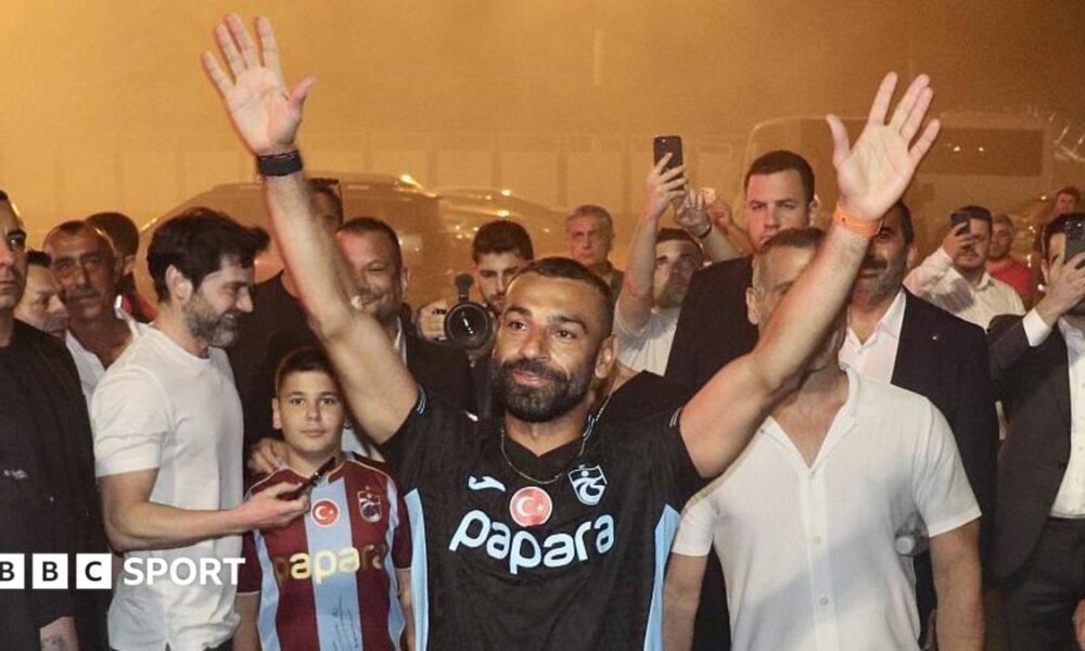 Mohamed Salah with a black Trabzonspor top on with his hands in the air outside Trabzon airport