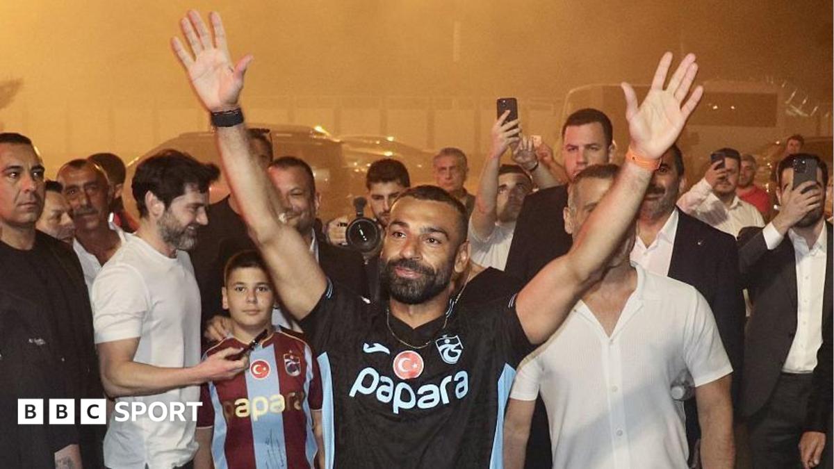 Mohamed Salah with a black Trabzonspor top on with his hands in the air outside Trabzon airport