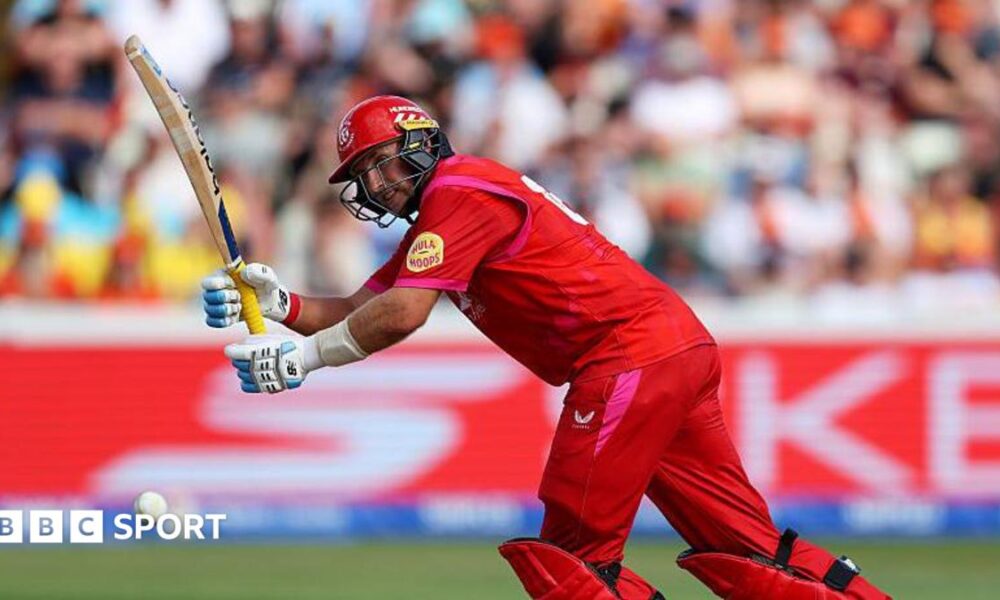 Joe Root, wearing red trousers, shirt and helmet, leans forward to play a shot with his bat held up in front of him
