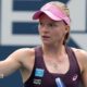 Harriet Dart, wearing a purple dress and pink visor, holds her racquet in her left hand and raises a clenched right fist